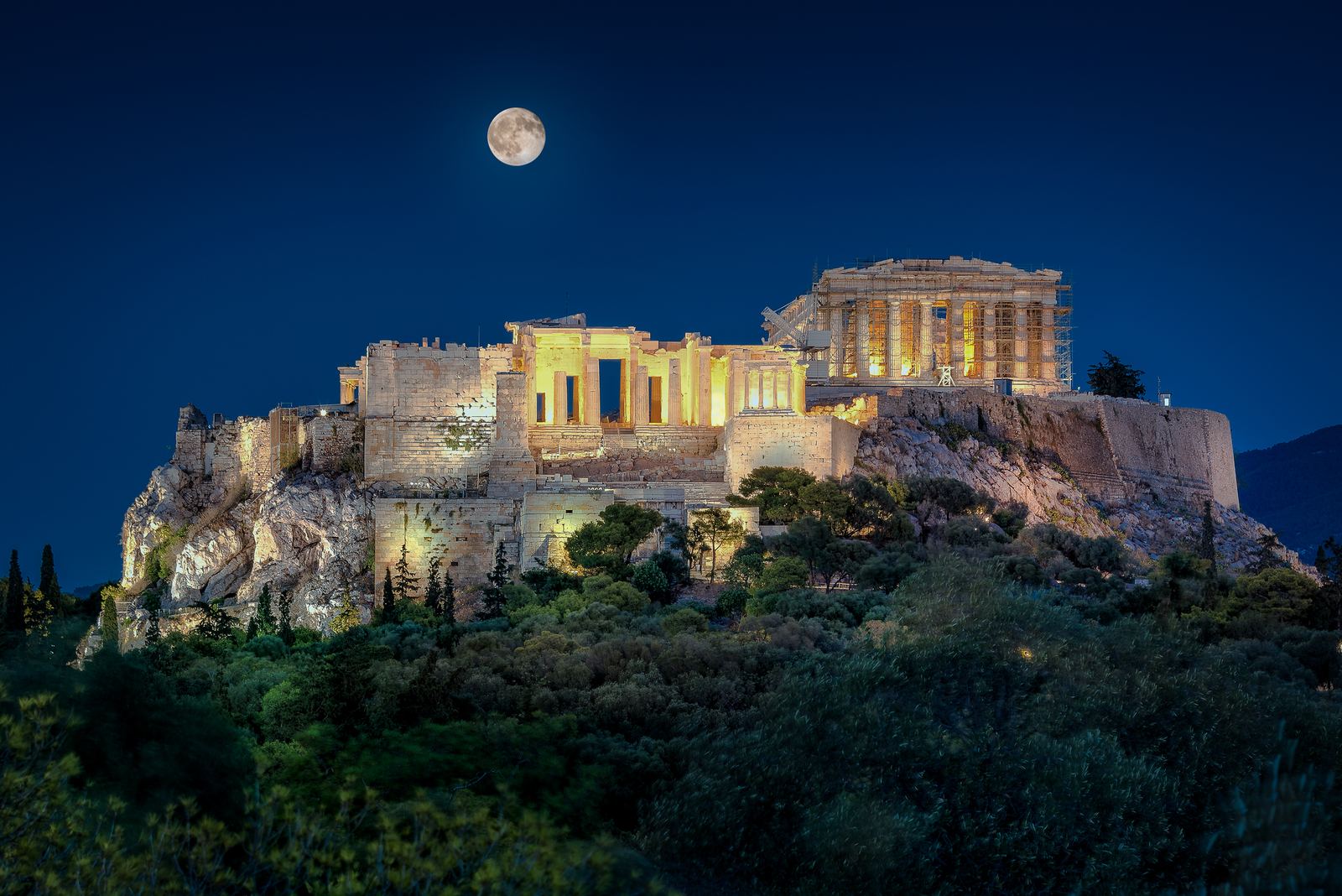 The Acropolis floodlit at night beneath a full moon